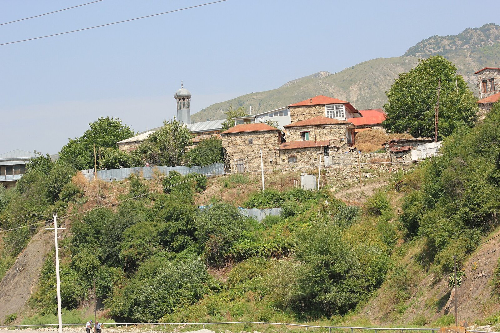Lahıcda təpə üzərində daş evlər və məscid minarəsi, aşağıda yol