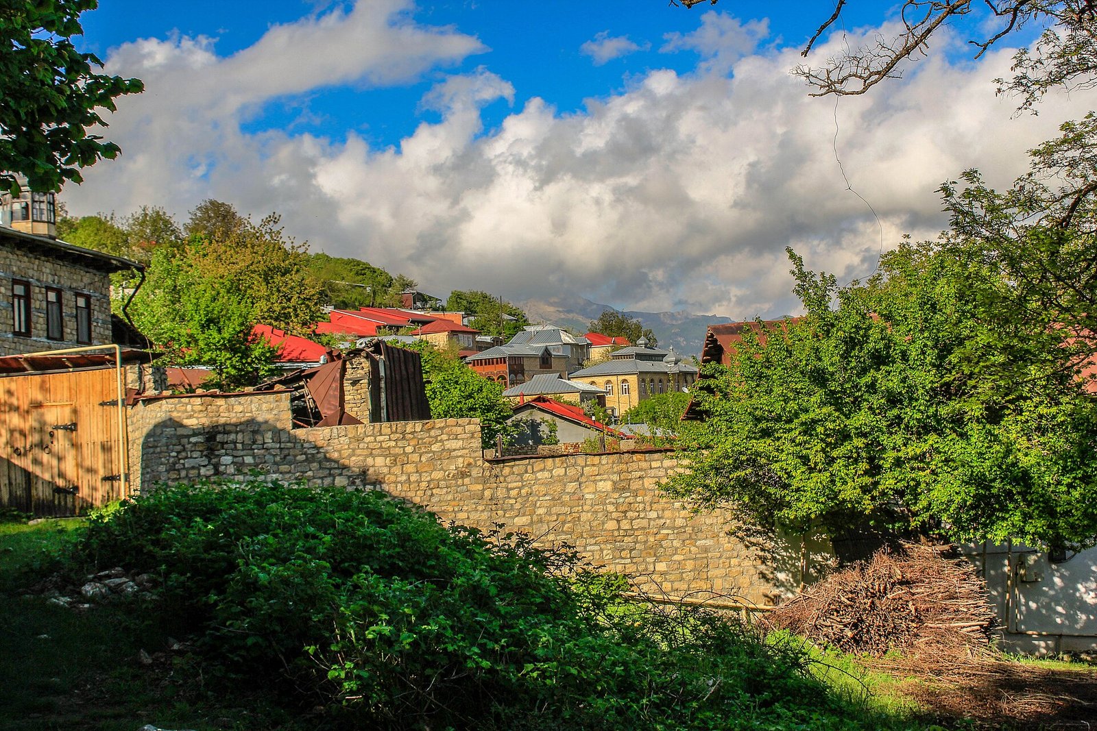 Basqal qəsəbəsində daş hasar və qırmızı damlı evlər, arxada dağlar
