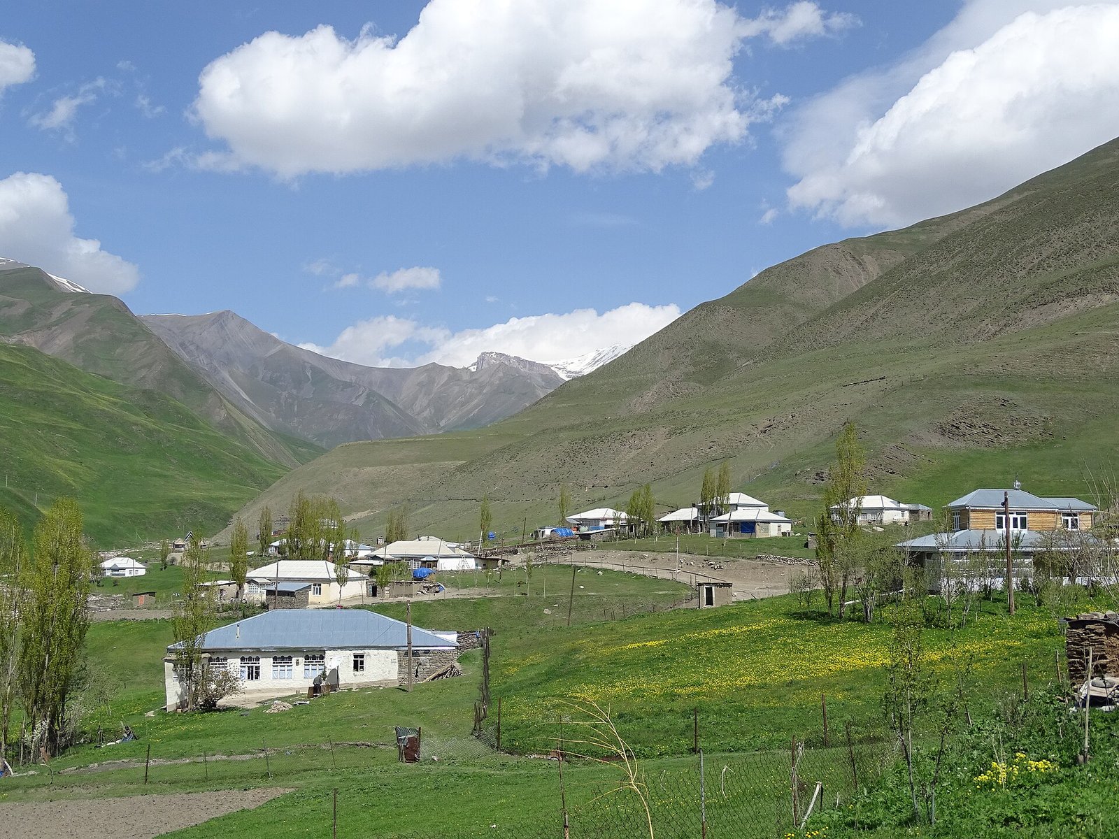 Xınalıq kəndinin evləri və yaşıl yamaclar, arxada qarlı Qafqaz zirvələri