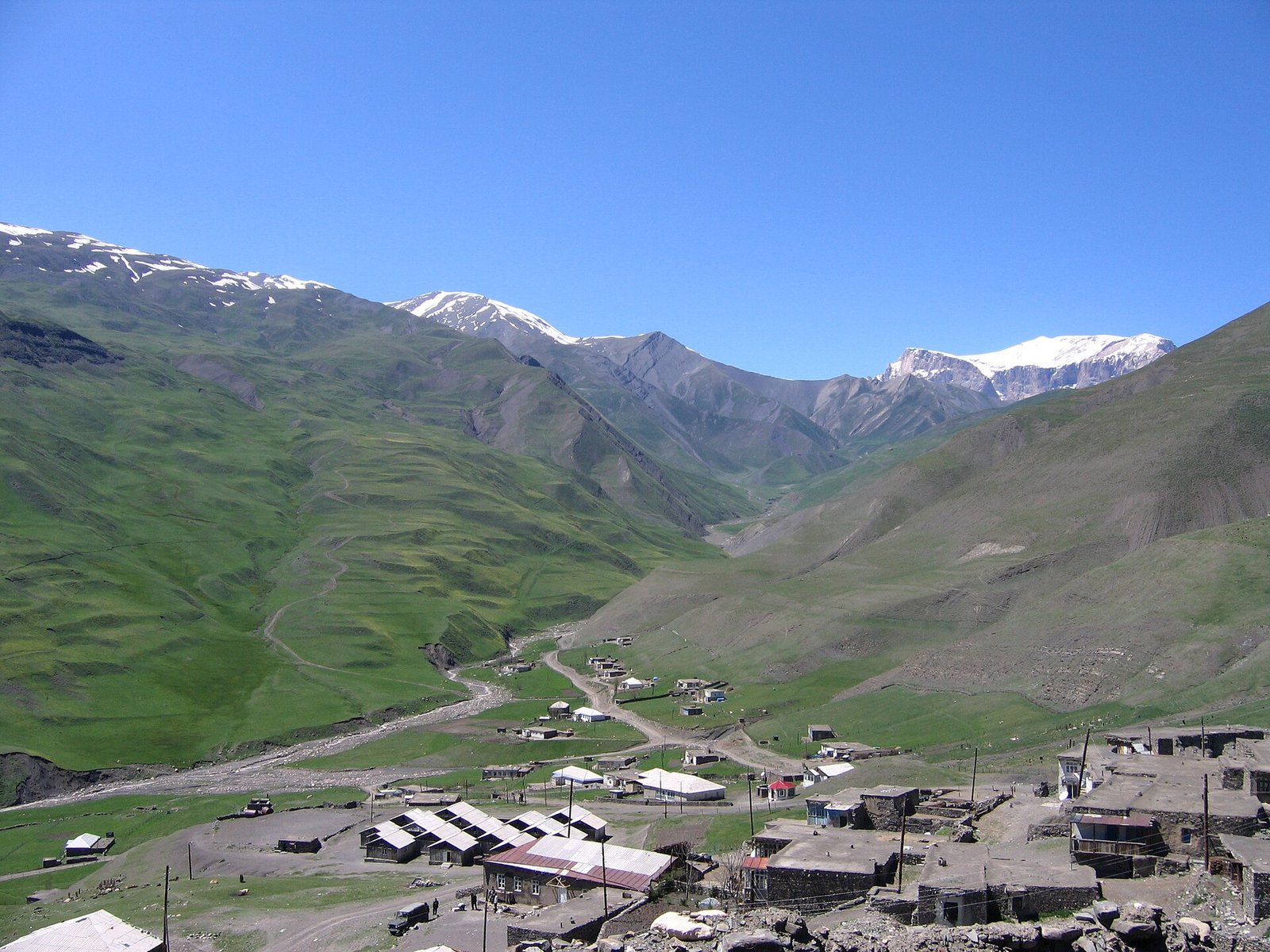 Xınalıq kəndinin evləri, arxada yaşıl dərə və qarlı Qafqaz zirvələri